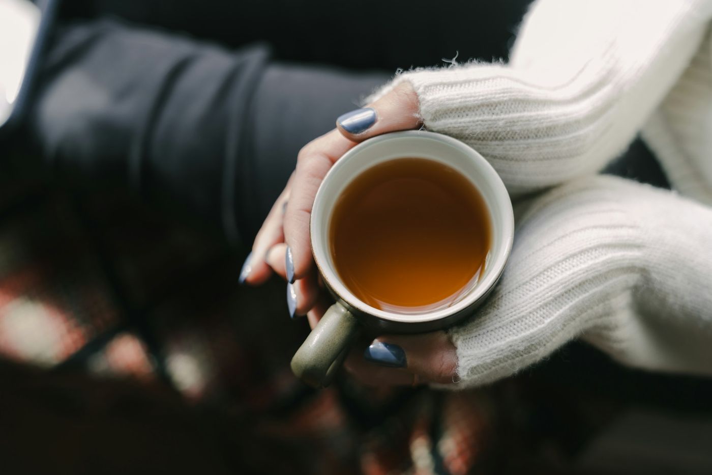 Two hands in a soft knit sweater holding a warm cup of tea.
